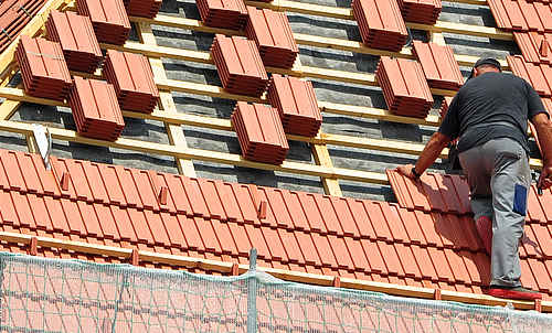Ein Arbeiter bedeckt ein Dach mit Ziegeln.