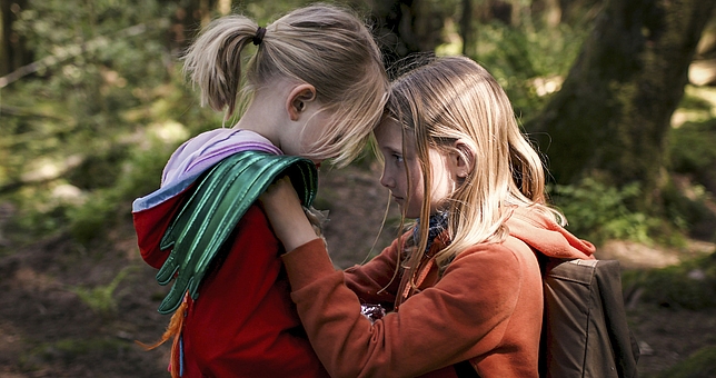 Zwei Mädchen stehen sich gegenüber und halten sich gegenseitig an den Schultern. Ihre Köpfe sind an der Stirn aneinandergelehnt.