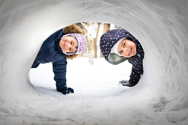 Zwei Mädchen schauen durch einen Tunnel aus Schnee in die Kamera.