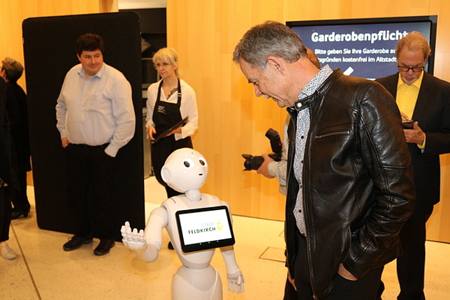 Ein Besucher blickt zum Pflegeroboter Pepper hinunter. Der Roboter blickt zum Besucher hoch.
