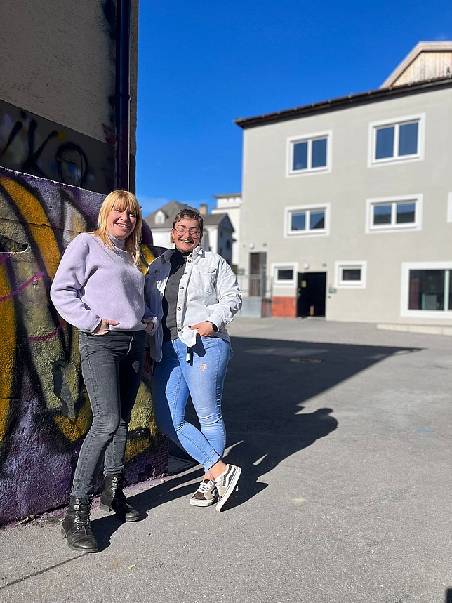 Zwei Frauen stehen nebeneinander vor dem Jugendhaus in Feldkirch und lehnen an eine Mauer.