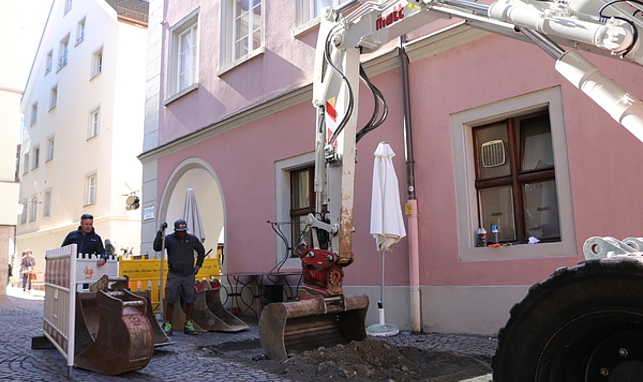 Ein Bagger bei Grabungen in der Schlossergasse, zwei Arbeiter stehen vor dem Bagger.