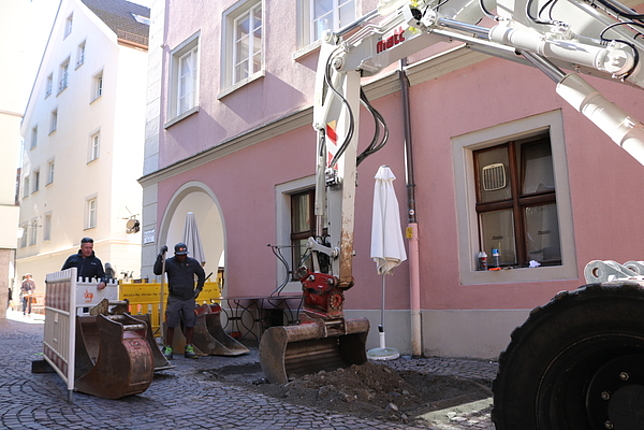 Ein Bagger bei Grabungen in der Schlossergasse, zwei Arbeiter stehen vor dem Bagger.