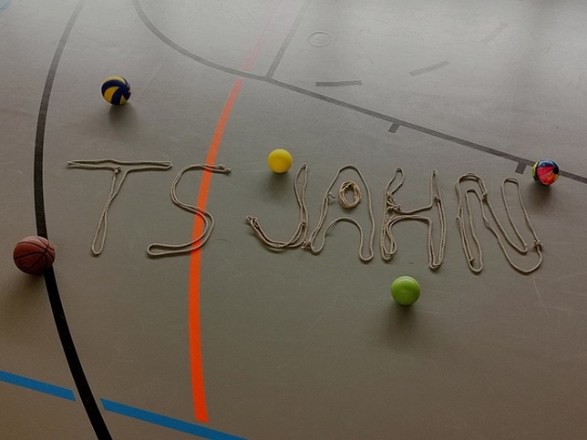 Der Schriftzug "TS Jahn" liegt mit Seilen geschrieben auf dem Turnhallenboden.