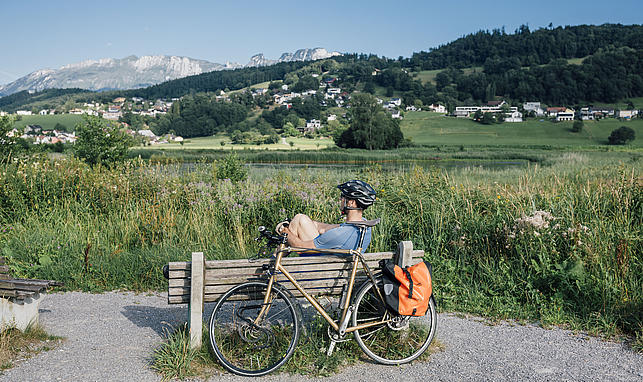 Ein Mann sitzt auf einer Holzbank am Egelsee. Er trägt einen Fahrradhelm und hinter dem Holzbank steht ein Fahrrad.