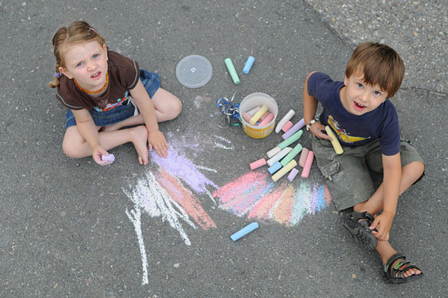 Zwei Kinder malen mit Straßenkreide auf die Straße 