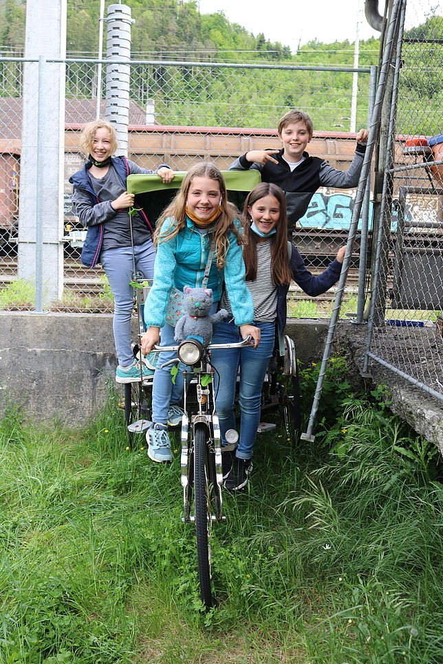 Drei Mädchen und ein Junge stehen bei einem Fahrrad. Im Hintergrund ist ein Güterwagon.