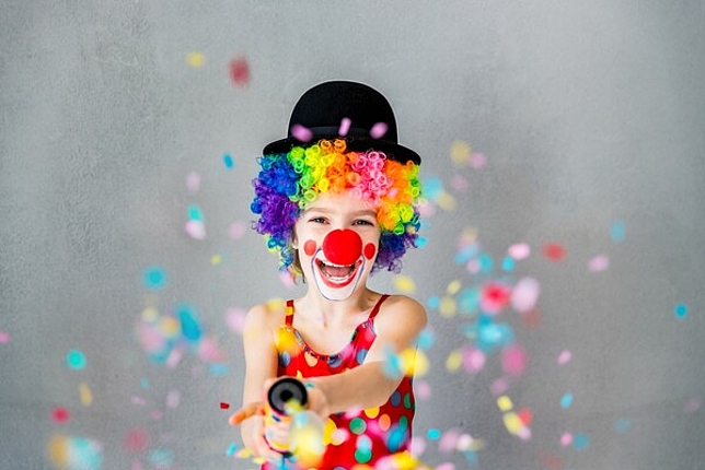 Ein kleines Kind ist als Clown verkleidet, lacht und verteilt Konfetti.