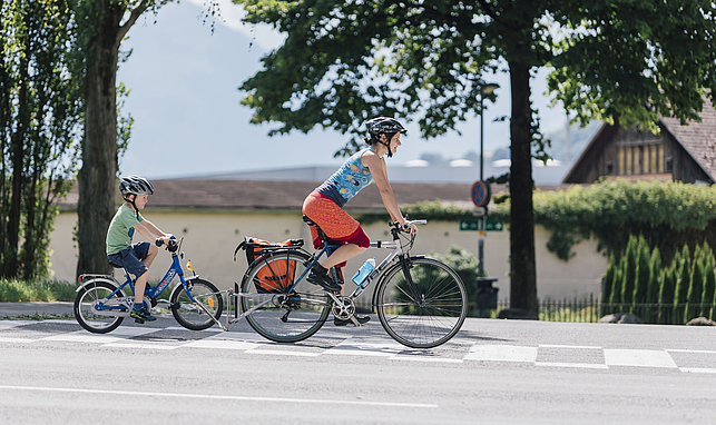 Eine Frau und ihr Kind fahren hintereinander mit dem Fahrrad auf einer Straße.