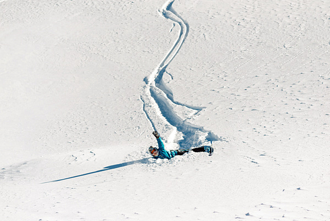 Ein Mädchen ist mit den Ski im Tiefschnee gefahren und hingefallen.