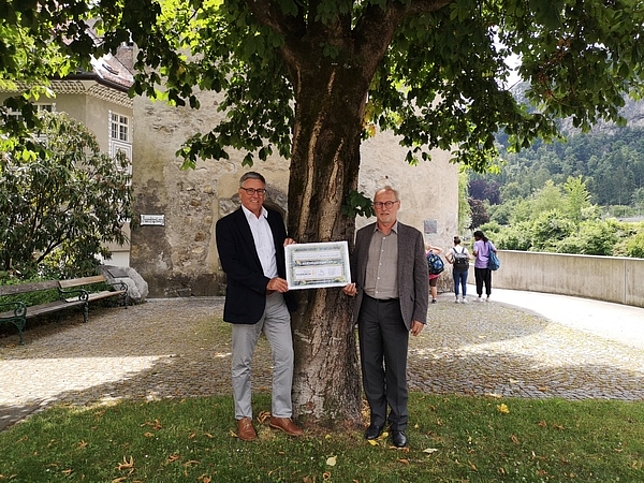 Bürgermeister Wolfgang Matt und Stadtrat Rainer Keckeis stehen vor einem Baum und halten die unterzeichnete Konvention in den Händen. 