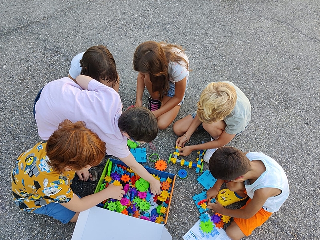 Kinder sitzen am Boden und setzen verschiedenformige Bauteile zusammen.