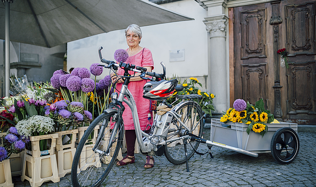 Eine Frau steht mit ihrem Fahrrad vor einem Blumenverkaufsstand.
