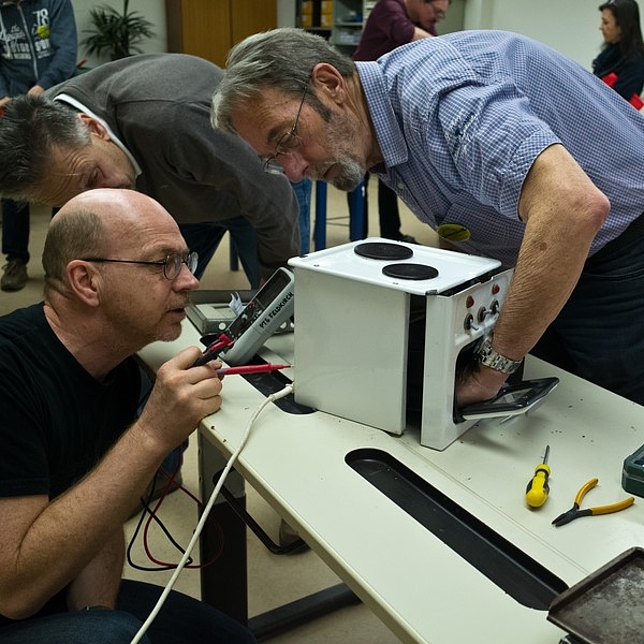 Drei Männer reparieren ein kleines Elektrogerät.