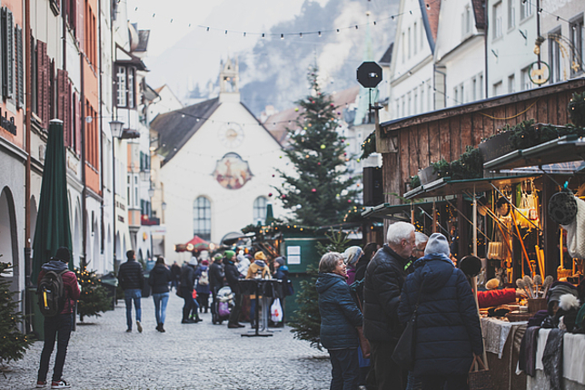 Einige Weihnachtsmarktstände stehen in der Marktgasse in Feldkirch und viele Leute bummeln über den Markt. 