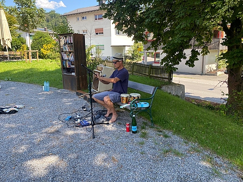 Ein Mann sitzt auf einem Holzbank, neben im liegen Instrumente, er richtet gerade ein Mikrofon aus.