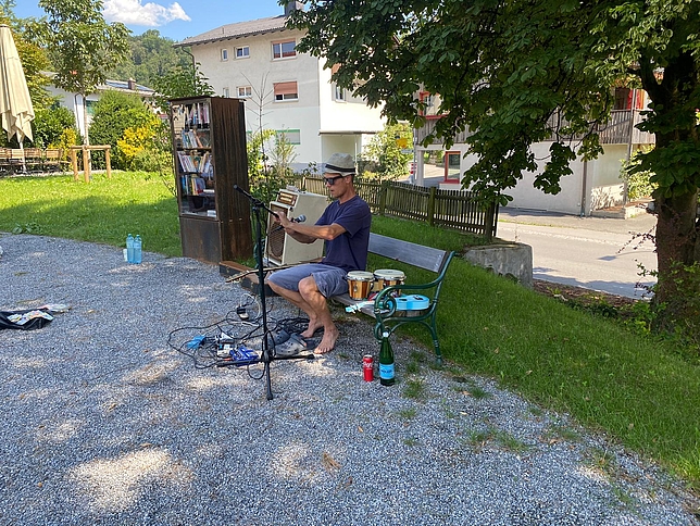 Ein Mann sitzt auf einem Holzbank, neben im liegen Instrumente, er richtet gerade ein Mikrofon aus.