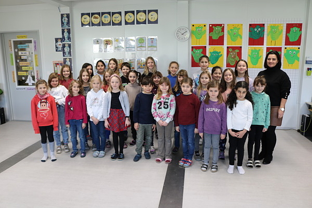Gruppenfoto mit Schüler:innen der Volksschule Altenstadt und Direktorin Monika Burtscher im Flurbereich ihrer aktuellen Schule.