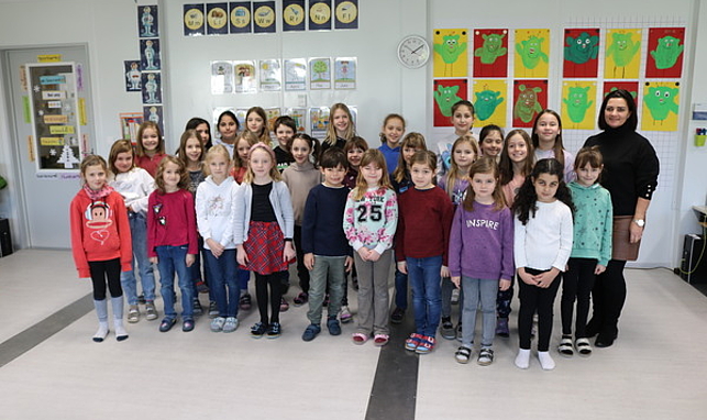 Gruppenfoto mit Schüler:innen der Volksschule Altenstadt und Direktorin Monika Burtscher im Flurbereich ihrer aktuellen Schule.