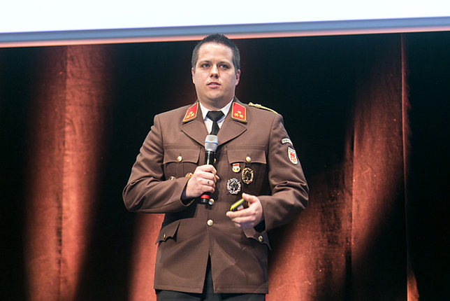 Kommandant der Feuerwehr Gisingen Dominik Leimegger steht auf der Bühne und spricht in ein Hand-Mikrofon.