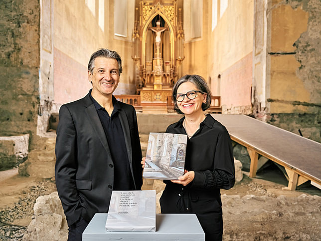 Die Herausgeber Arno Egger und Karin Guldenschuh posieren mit dem Buch in der Johanniterkirche.