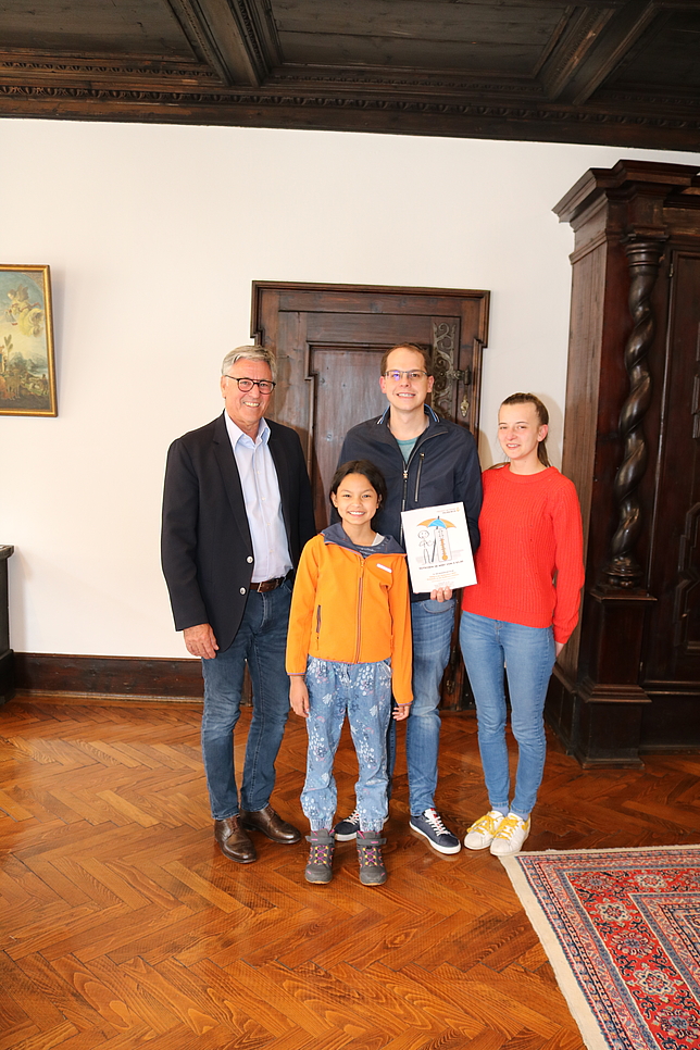 Bürgermeister Matt mit Gewinner Manuel Enzenhofer, einem kleinen Jungen und einer Frau bei der Übergabe des gewonnenen Gutscheins.