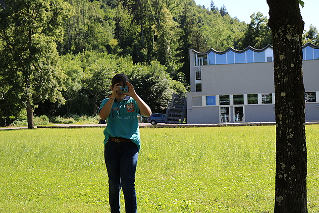 Ein Mädchen steht mit einer Kamera vor dem Gesicht im Reichenfeld. 