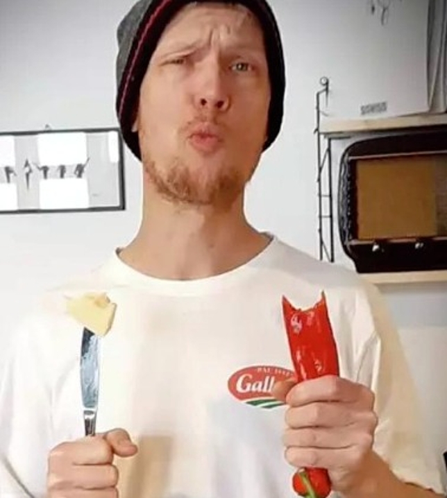 Ein Mann hält in der einen Hand ein Messer mit Butter und in der anderen eine angebissene Chilli.