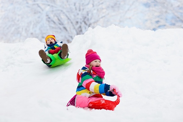Zwei kleine Kinder rutschen einen Schneehügel hinunter.