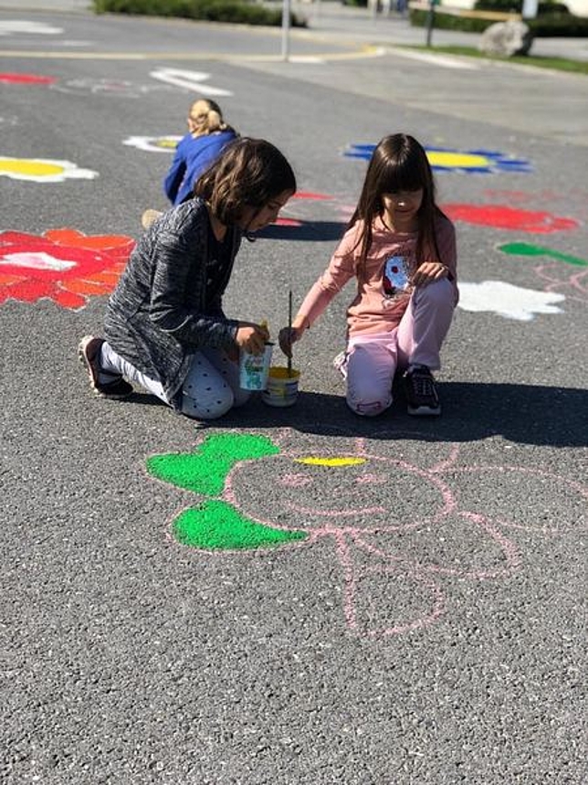 Zwei Mädchen malen eine Blume auf die Straße
