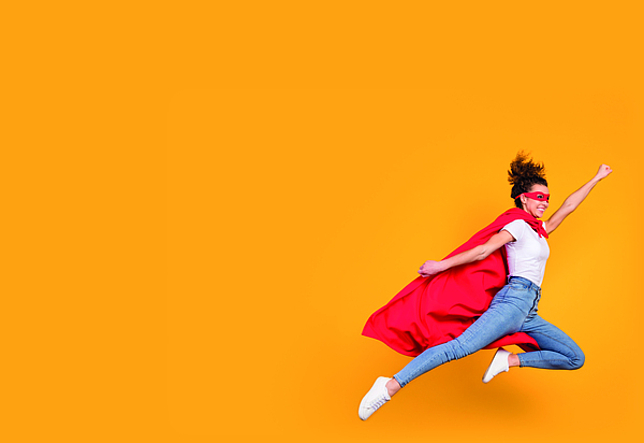 Eine Frau ist als Superheldin verkleidet und springt in die Luft. 