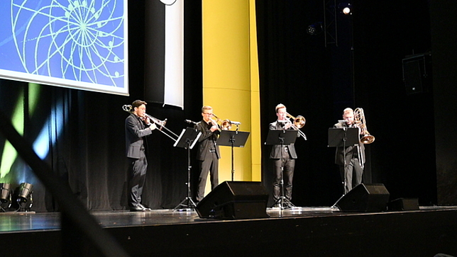 Vier junge Männers stehen auf der Bühne und spielen Posaune.