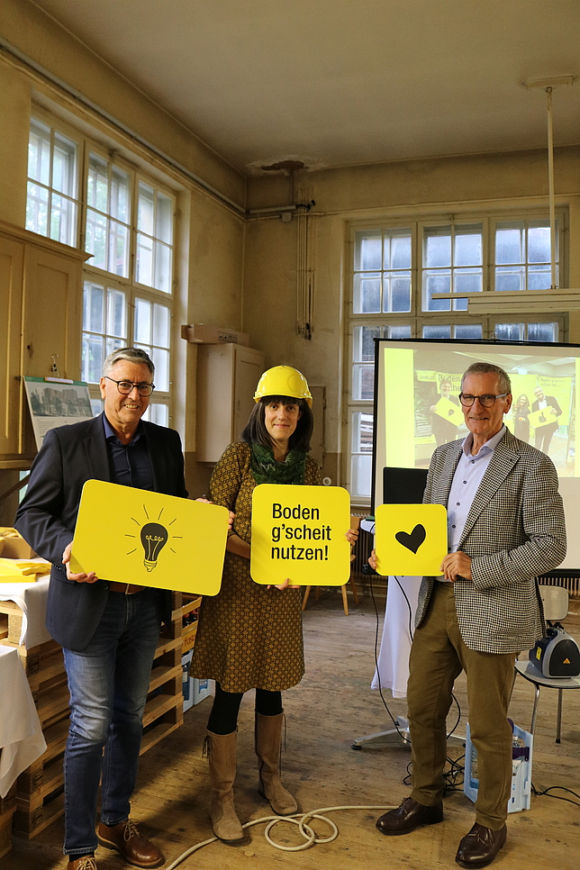 Bürgermeister Wolfgang Matt, Felicitas Baldauf und Josef Mathis vom Verein "LandLuft" halten gelbe Schilder.