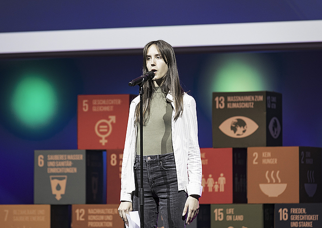 Ein junges Mädchen steht auf der Bühne und spricht in ein Mikrofon.