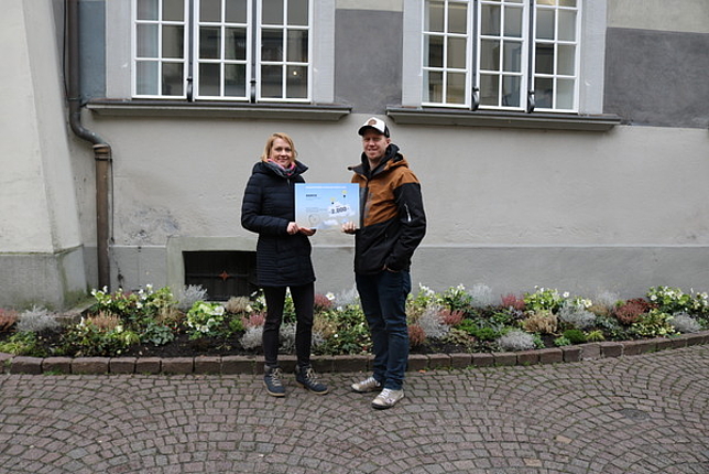 Anne Schade und Beat Delpin von der Offenen Jugendarbeit Feldkirch halten einen Scheck in Höhe von 2.000 Euro in den Händen. Sie stehen draußen vor dem Rathaus.