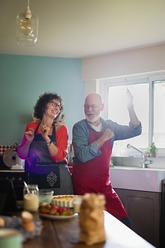 Ein älterer Herr und eine ältere Dame stehen in der Küche und lachen.