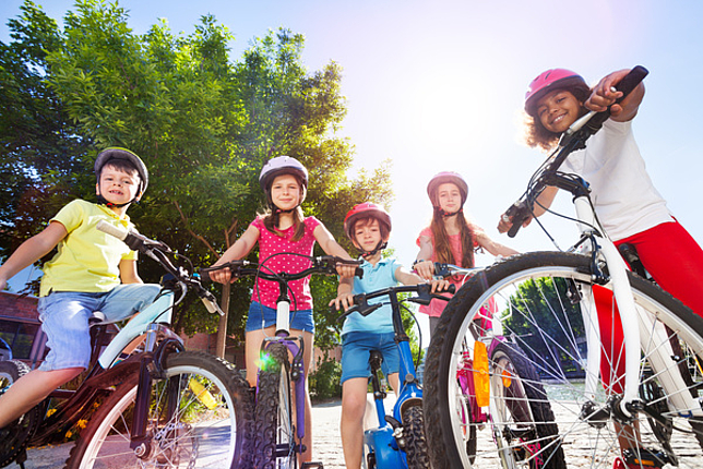 Eine Gruppe glücklicher Kinder steht mit ihren Fahrrädern und Sicherheitshelmen in einemPark.
