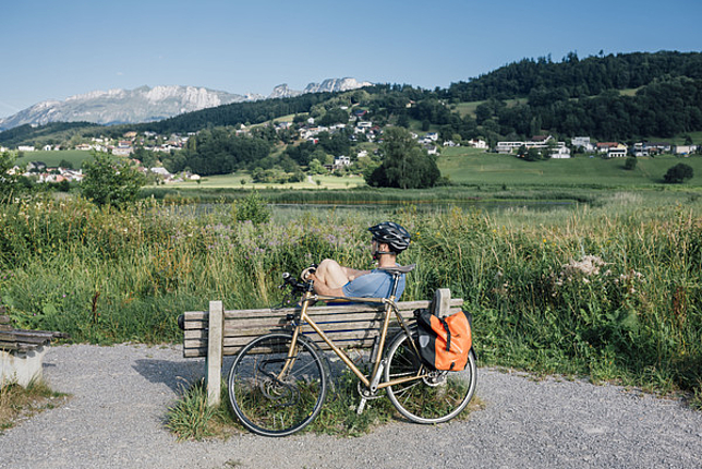 Ein Mann sitzt auf einer Holzbank am Egelsee. Er trägt einen Fahrradhelm und hinter dem Holzbank steht ein Fahrrad.