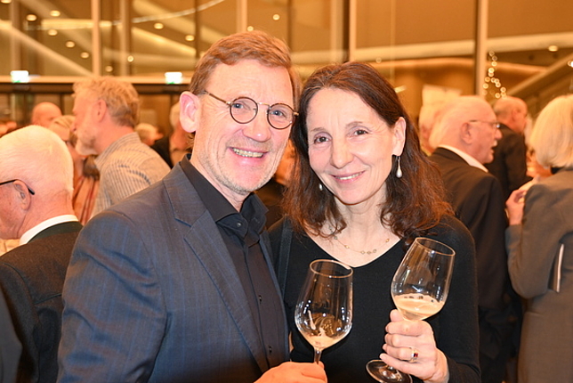 Ein Mann und eine Frau stehen nebeneinander, beiden halten je ein Weinglas in der Hand.