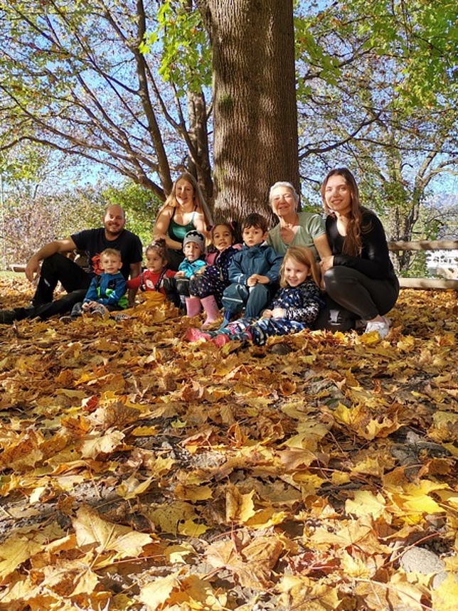 Die Kinder und Pädagog:innen der Outdoorgruppe Tisis Carina sitzen unter einem Baum im Laub.