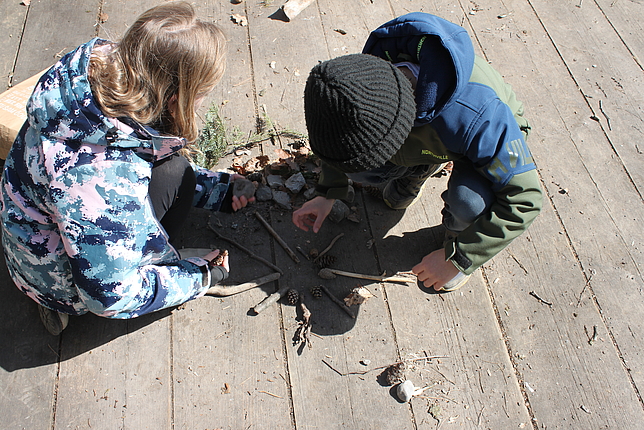 Zwei Kinder legen auf einem Holzboden ein Bild aus Naturmaterialien
