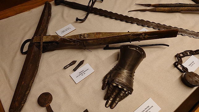 Die Hand einer Ritterrüstung sowie Teile einer Jagdausrüstung auf einem Tisch
