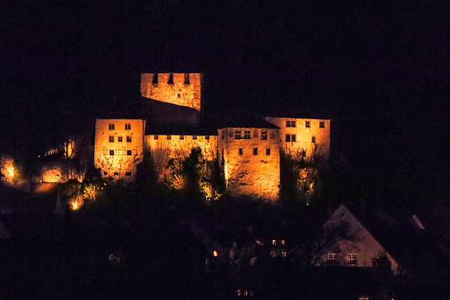Die Schattenburg bei Nacht. Die Burg erstrahlt in orangem Licht. 