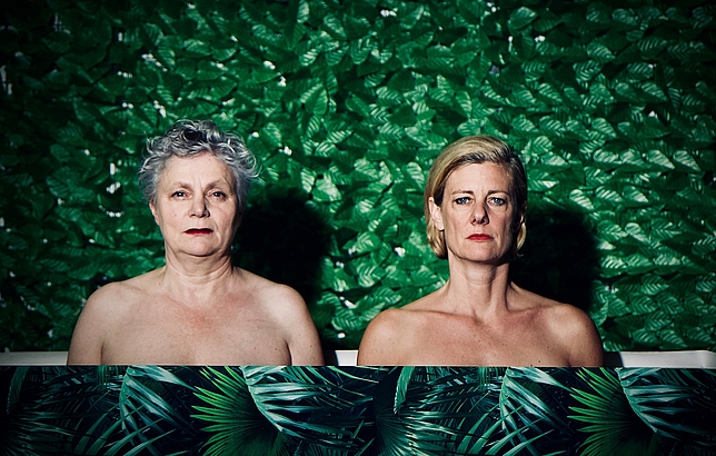 Zwei Damen stehen mit ernster Miene vor einem grünen Hintergrund