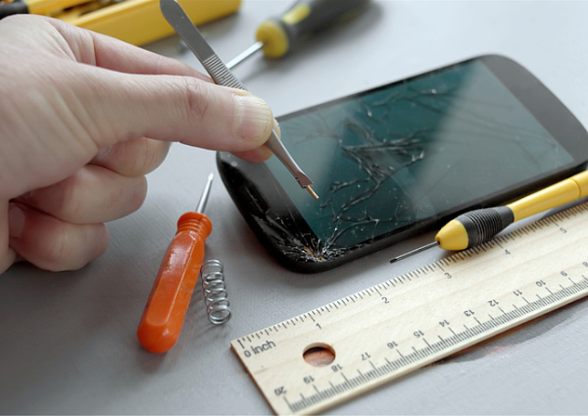 Ein kaputtes Handy wird mit entsprechendem Werkzeug repariert.