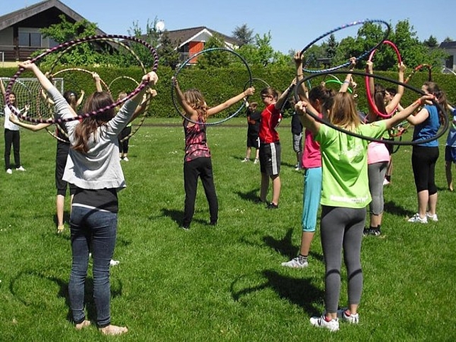 Viele Kinder stehen mit einem Hula Hoop auf einer Wiese.
