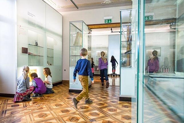 Einige Kinder laufen durch das Museum und einige Kinder betrachten Ausstellungsstücke in den Glasvitrinen.