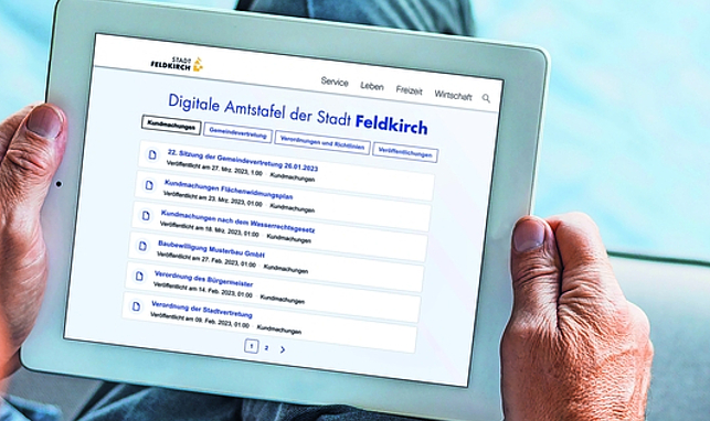 Eine Person hält ein Tablet, auf dem die Digitale Amtstafel der Stadt Feldkirch zu sehen ist.