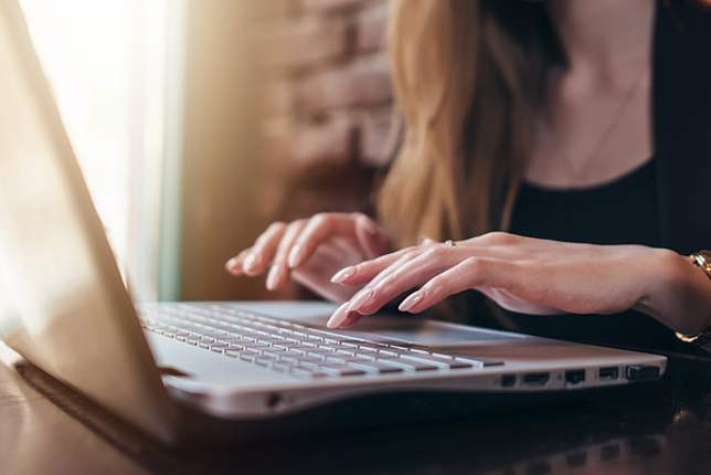 Eine Dame sitzt am Laptop, ihr Hände tippen auf der Tastatur.